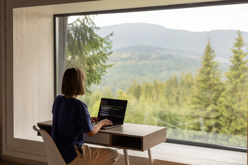 Remote worker looking out the window and viewing a lush landscape of trees and mountains