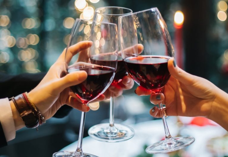 Three people toasting with wine glasses full of red wine