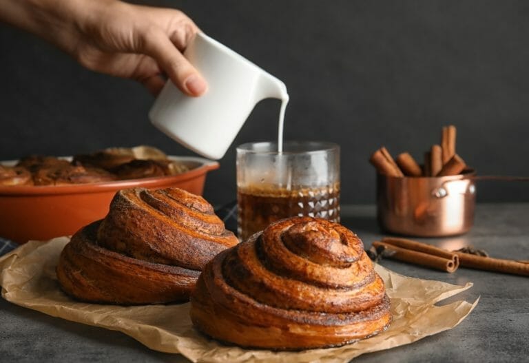 Someone pouring cream into a glass mug of coffee surrounded by baked goods from Tartine Bakery