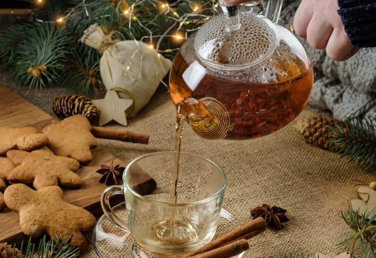 Someone holding a glass teapot pouring tea into a mug with a festive holiday background