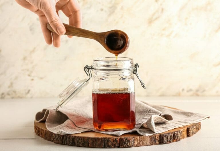 A wooden spoon dripping maple syrup into a glass mason jar
