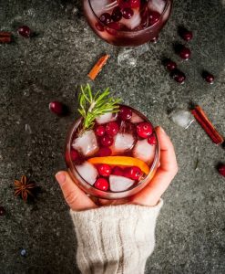 A person's hand holding a vibrantly colored festive holiday cocktail