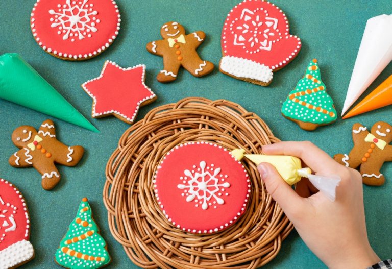 Close up of someone decorating a festive red holiday cookie with a white snowflake design
