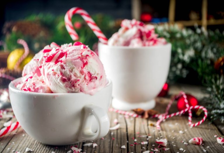 Two mugs full of ice cream topped with candy cane pieces and a festive background of garlands 