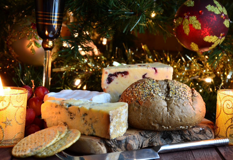 Several types of cheese surrounded by bread with a background of garlands and holiday ornaments 