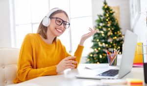 Remote worker sitting at a desk and smiling during a video conference with a festive holiday tree in the background.